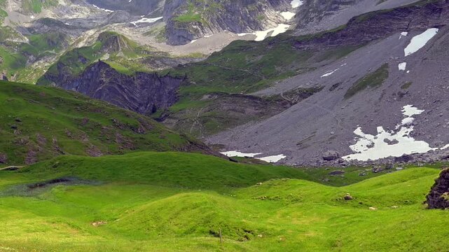 Lush green mountain valley with rugged rocky slopes and lingering summer snow in the Swiss Alps near Axalp.