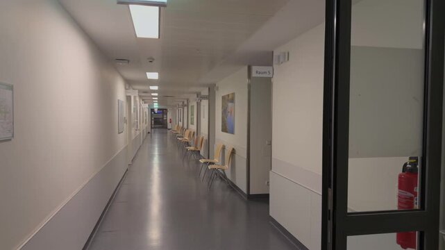 Empty hospital corridor in Germany at night with clean modern interior, chairs along the wall and bright lighting. Quiet clinical environment with no people, showing healthcare facility stillness.