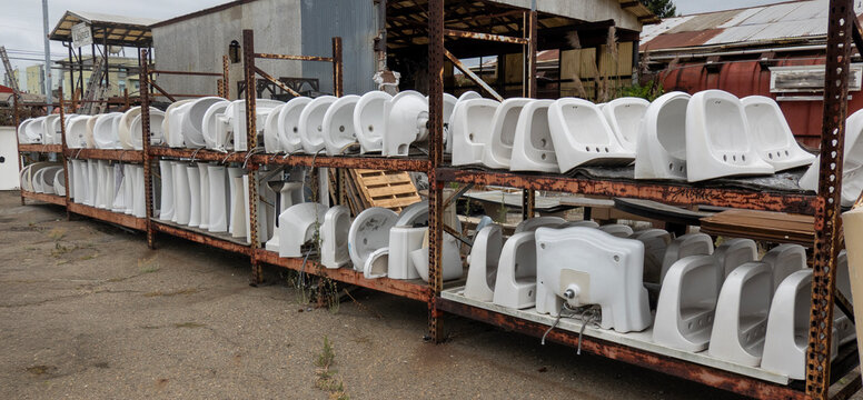used sinks-Rows of salvaged white ceramic sinks and pedestals are neatly organized on outdoor metal shelving racks for resale.