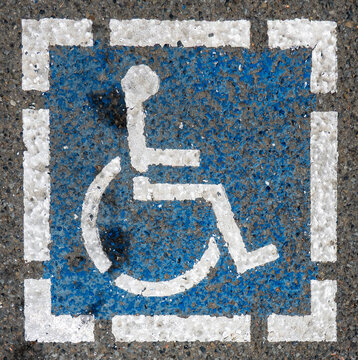 weathered handicapped sign-A weathered blue and white international symbol of accessibility is painted directly onto rough asphalt pavement.