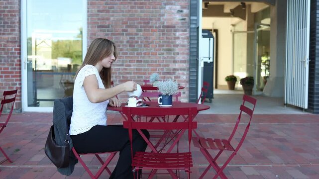 Woman waits alone at outdoor cafe for a man who is late for their date pouring tea and growing impatient as time passes with no sign of him while dessert sits untouched