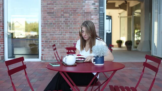 Woman on diet holds a slice of cake close to her face at outdoor cafe looking upset as she struggles with dessert cravings self control and healthy eating goals for today