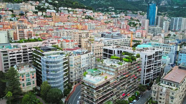 Drone view of Monaco cityscape from above. Dense residential buildings, narrow streets and the mountain backdrop create a compact luxury urban panorama.