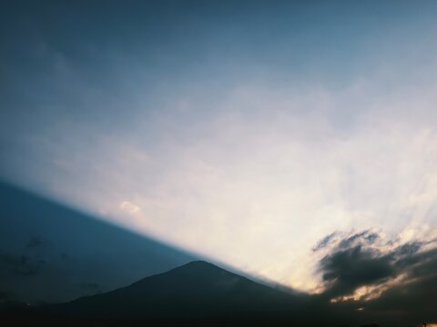 Majestic silhouette of Mount Fuji at dusk with dramatic sunset light and soft clouds in blue sky