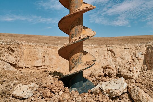 Heavy spiral auger drilling into gritty packed soil and fractured rock, featuring rusted metal textures for geotechnical and construction campaigns