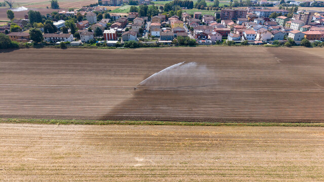 Aerial view of a travelling sprinkler system irrigating crops across an agricultural field, showcasing modern farm irrigation and water management in Mediglia, Lombardy, Italy.