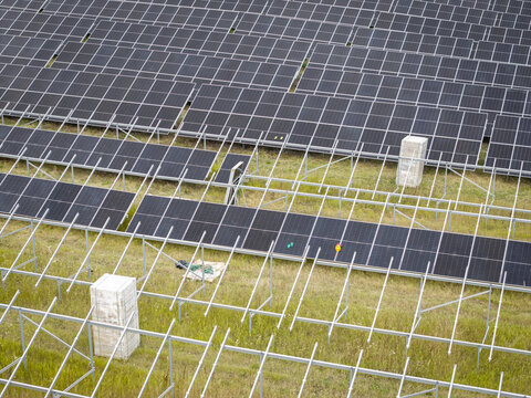 Aerial view of a solar farm under construction with rows of photovoltaic panels being installed on metal frames in a grassy field in Poland.