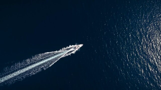 High aerial overhead tracking view of a RIB motorboat driving with speed over blue ocean