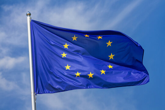Flag of the European Union waving in the wind on flagpole against the sky with clouds on sunny day, close-up