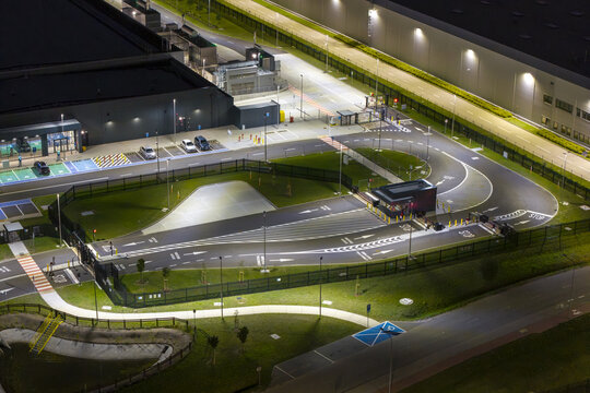 Aerial view of an AI data center at night, featuring a secure entrance gate, illuminated parking area, and modern industrial facility buildings in Poland.