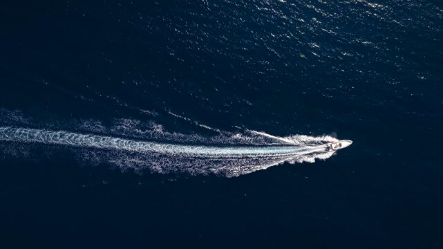Aerial overhead view of a RIB motorboat cruising in a circle over the blue ocean and out of the frame