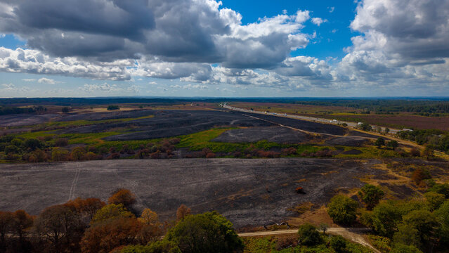 Aerial view of the A31 New Forest wildfire burn scar in New Forest National Park, showing charred landscape, green patches, and the adjacent highway in New Forest District, England, United Kingdom.