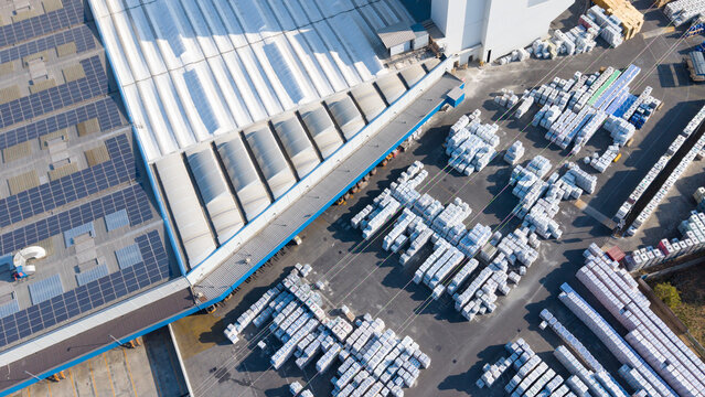 Aerial view of a manufacturing facility for building materials, featuring warehouse roofs with solar panels and organized stacks of supplies in Peschiera Borromeo, Lombardy, Italy.
