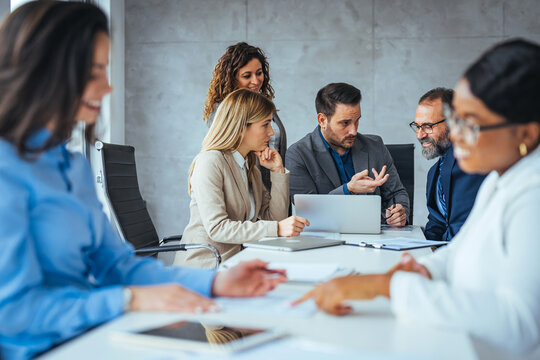Business Meeting Team Discussing Strategy Around Laptop in Modern Office Conference Room