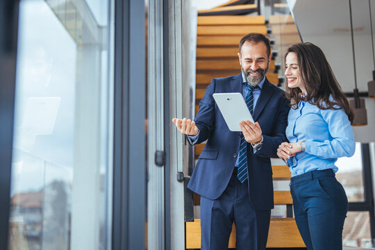 Smiling Business Colleagues Reviewing Tablet Together in Modern Office Stairwell During Meeting