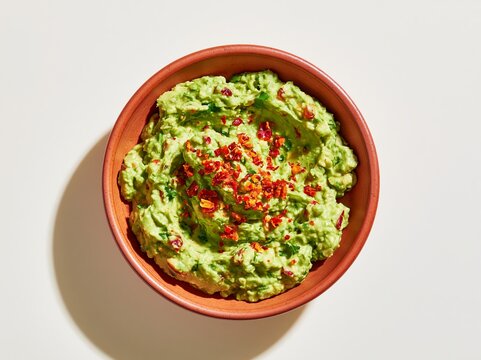 Guacamole in a terra rossa bowl topped with red chili flakes, placed on a light background, showcasing a vibrant and fresh culinary dish ideal for appetizers or dips