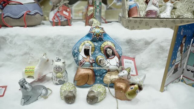 Centered handpainted blue nativity block depicting stylized Mary, Joseph, and infant with gold halos and star, arranged on white faux-snow and surrounded by small painted animal ornaments including