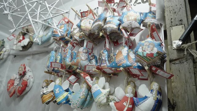 Handmade textile Christmas ornaments shaped like stars, bells, angels, and dolls hang from wooden peg displays in market stall holiday craft display, fabric textures visible as ornaments sway