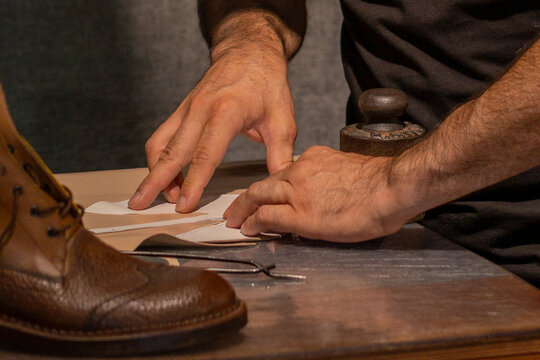 Artisan shoemaker cutting leather on workbench with shoe in progress and tools