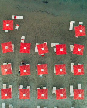 Aerial view of rows of vibrant red beach umbrellas and lounge chairs neatly arranged on the sandy beach in Cupra Marittima, Marche, Italy.