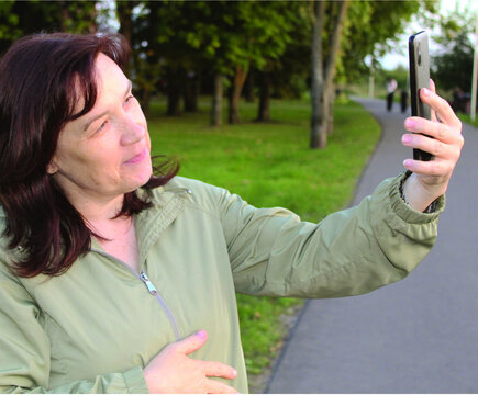 Happy Mature Woman Taking Selfie with Smartphone in Green Park.

