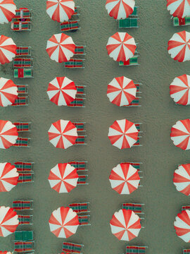 Aerial view of rows of red and white striped beach umbrellas and sun loungers on the sandy beach in Cupra Marittima, Marche, Italy.