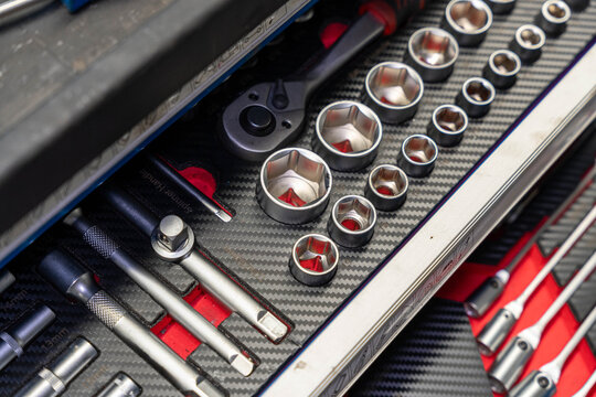 Socket wrench assortment fills tool drawer with ratchets, extensions, and polished sockets secured in fitted slots. Red accents and dark carbon fiber surface support garage maintenance tasks.