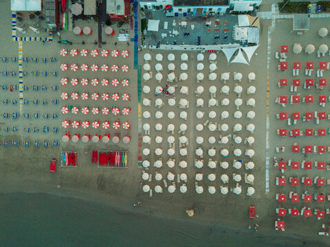 Aerial view of organized rows of colorful beach umbrellas and sun loungers on the sandy coastline of Cupra Marittima, Marche, Italy.