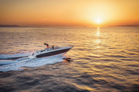 Side view of a sports motor boat cruising with speed over calm into the colorful sunset