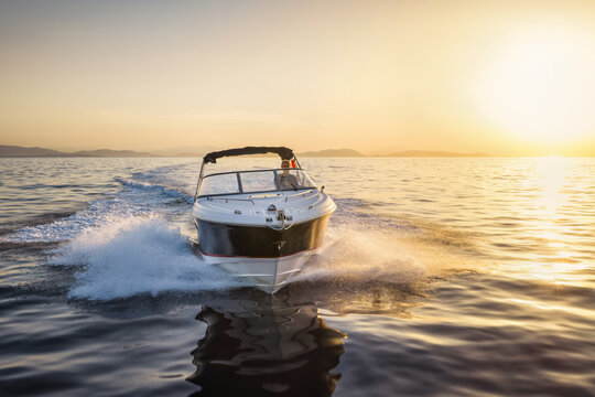 Front view tracking of a motor speedboat cruising over the calm ocean during golden sunset time