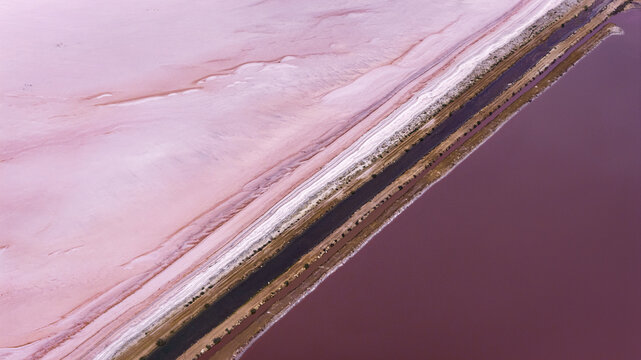 Aerial view of the pink salt lake showing the industrial geometry of salt factory channels and vibrant mineral-rich water in Denham, Western Australia, Australia.