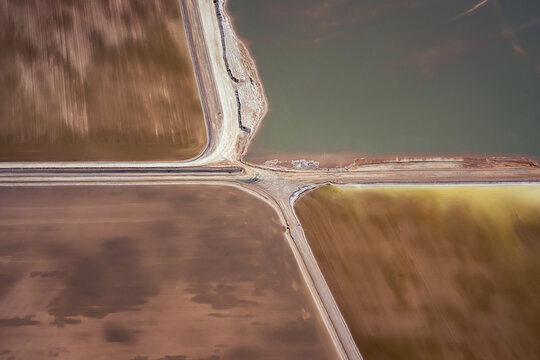 Aerial view of the industrial geometry of salt lake evaporation ponds with contrasting earth tones and textured water surfaces in Denham, Western Australia, Australia.