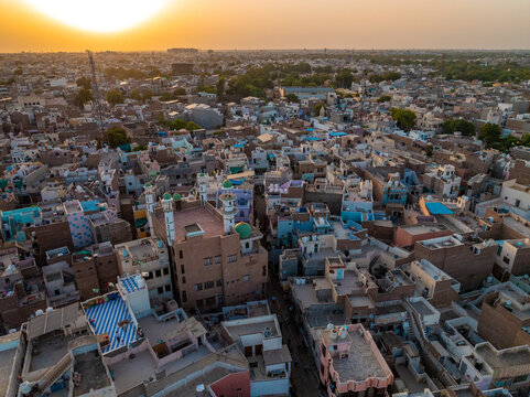 Aerial view of the dense urban landscape featuring a mosque with green domes, flat-roofed buildings, and narrow streets bathed in golden sunset light in Bikaner, Rajasthan, India.