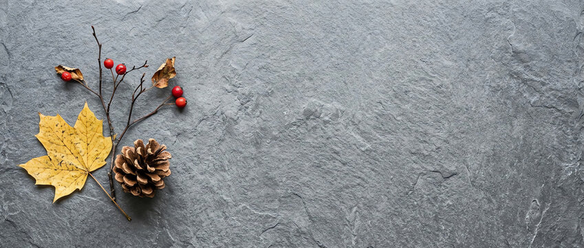 Autumn flat lay banner with yellow maple leaf, pine cone, and red berries on grey slate stone background, minimalist seasonal composition with copy space for natural home decor.