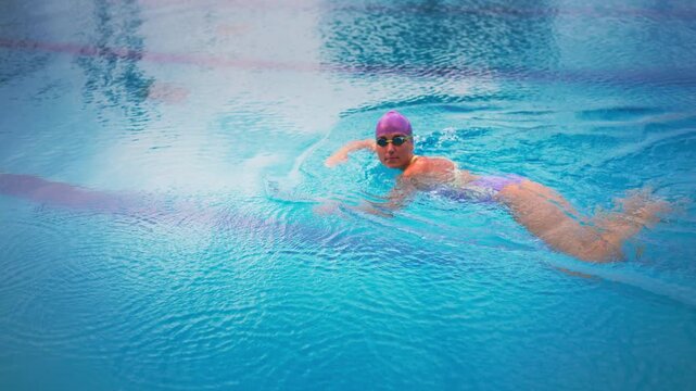 Determined female athlete training in outdoor swimming pool, pushing off wall and powering into freestyle stroke, showcasing physical performance, endurance, strength, focus and competitive mindset