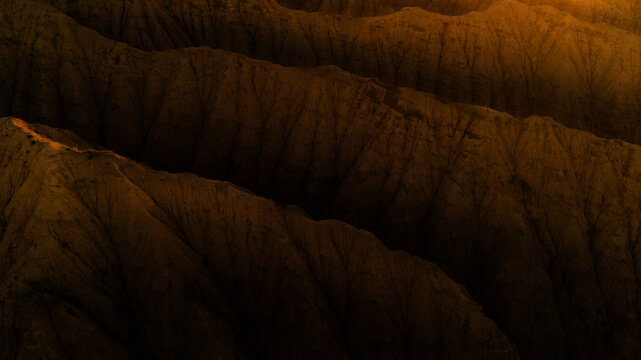 Aerial view of the rugged, eroded mountain ridges of Ak-Say Valley with dramatic shadows and golden light highlighting the textured slopes in At-Bashi District, Naryn Region, Kyrgyzstan.