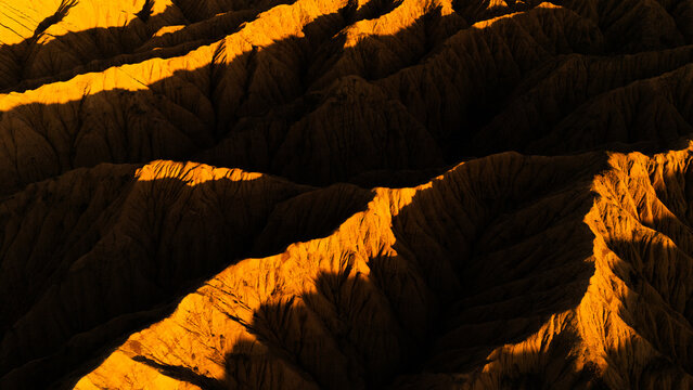 Aerial view of the rugged, golden-lit ridges and deep shadows of the Ak-Say Valley in At-Bashi District, Naryn Region, Kyrgyzstan.
