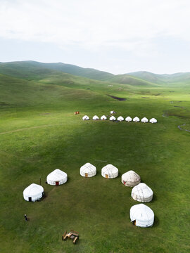 Aerial view of the Song-Kul yurt camp featuring a circular arrangement of white yurts on a vast green meadow surrounded by rolling hills in Naryn Region, Kyrgyzstan.