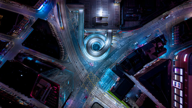 Aerial view of the illuminated spiral parking ramp at night, with surrounding city streets, traffic light trails, and urban architecture in Manchester, England, United Kingdom.