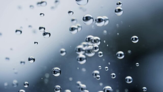 Slow motion static macro view of water bubbles rising and drifting in glass tank with blurred blue grey background
