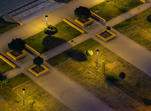 Aerial view of the Morasko university parking lot at night, featuring illuminated pathways, manicured trees in planters, and geometric landscaping in Poznan, Greater Poland Voivod, Poland.