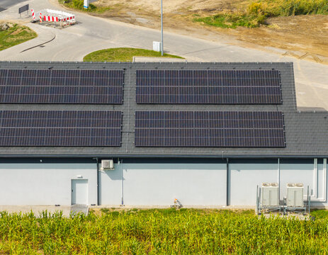 Aerial view of solar panels installed on the roof of a modern commercial building with HVAC units and a cornfield in the foreground in Poznan, Greater Poland Voivod, Poland.