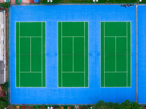 Aerial view of three green tennis courts with blue surrounding surfaces in Market Harborough, England, United Kingdom.