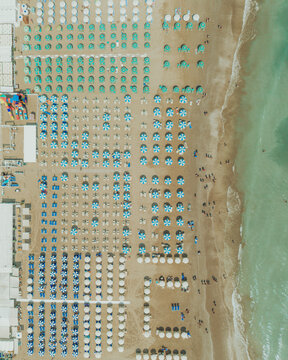 Aerial view of rows of colorful beach umbrellas and sun loungers on the sandy beach in Senigallia, Marche, Italy.