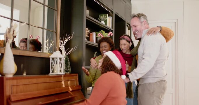 Diverse friends leaning and singing while Santa hat pianist starting holiday tune at upright piano