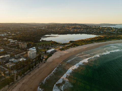 Aerial view of Dee Why Beach and the adjacent lagoon at golden hour with waves breaking on the sandy shore and residential buildings in Dee Why, New South Wales, Australia.
