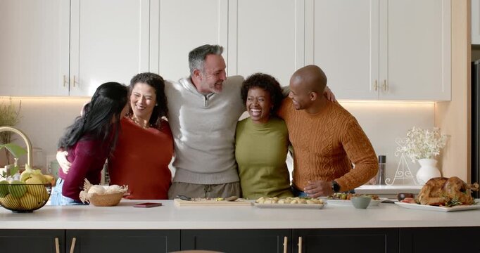 Diverse friends linking arms, laughing at kitchen island, celebrating meal with roasted bird