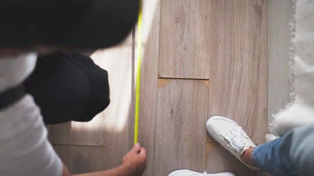 High-angle view of a contractor using a measuring tape on a new wooden floor, then writing down the dimensions on a clipboard, providing a quote for a home improvement project