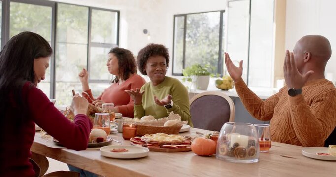 Diverse family at table in sweaters laughing as Asian woman offering bite with fork from roast