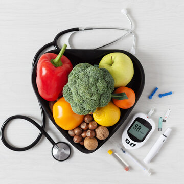 Healthy diet concept with heart shaped bowl of fresh vegetables fruits nuts and medical equipment including blood glucose meter for diabetes management top view PNG transparent background